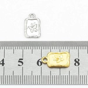 Detail view of gold and silver butterfly rectangle pendants with measurement scale