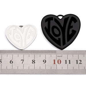 Macro detail of large heart pendants with LOVE relief and size reference on a steel ruler