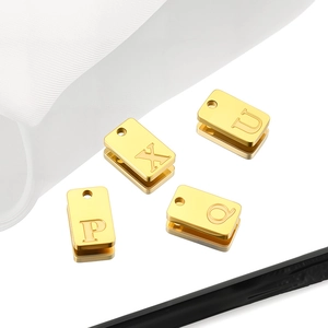 Macro detail of four gold stainless steel square charms with engraved letters P, X, U, and Q