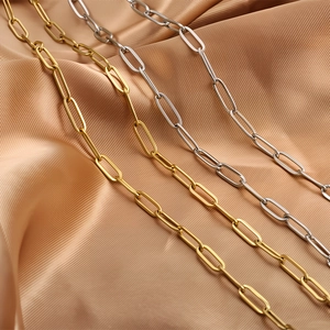 Detailed view of gold and silver stainless steel paperclip chains on champagne silk fabric