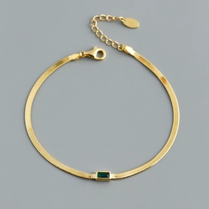 Detail eines goldenen Schlangenkette-Armbands mit einem rechteckigen grünen Zirkon