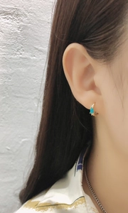 Close-up of a gold hoop earring featuring a turquoise drop stone and pave accents