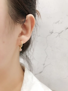 Détail d'une boucle d'oreille dorée avec petits zircons et pierre rose sur une oreille