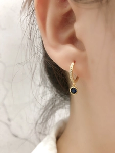 Détail de créoles dorées avec petits cristaux et pendentif rond en pierre bleue foncée
