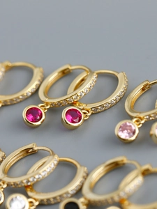Gros plan de créoles dorées avec pavé de zircons et pendentifs en pierres colorées