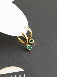 Vue macro de boucles d'oreilles créoles dorées avec zircons et pendentif pierre verte ronde