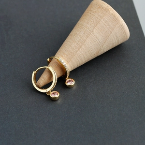 Détail de boucles d'oreilles dorées avec diamants blancs et pendentifs en pierre rose