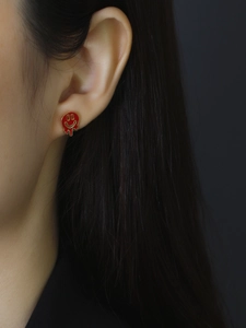 Close-up of a melting red smiley face stud earring with golden metal edge on ear