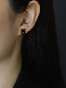 Close-up of a melting smiley face stud earring in black and gold on a model's ear