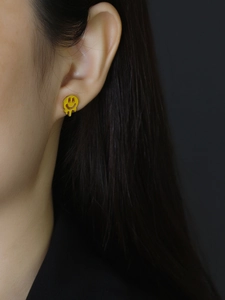 Close-up of a melting yellow smiley face stud earring in 925 sterling silver worn on ear