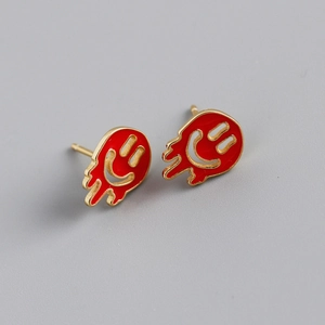 Macro detail of melt smile face stud earrings with red enamel and gold plating