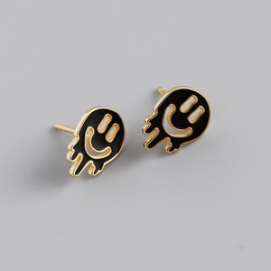 Detail shot of melting smiley face earrings with gold trim and black enamel finish