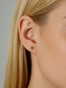 Close-up of minimalist square gold stud earring with green zircon on model's ear