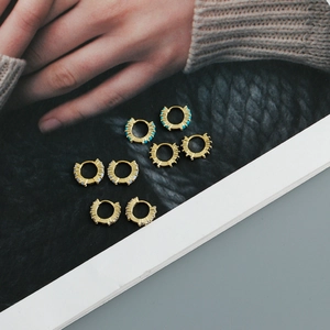 Détail de boucles d'oreilles créoles dorées ornées de turquoises, opales et pierres noires