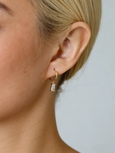 Gros plan d'une boucle d'oreille dorée avec zircon rectangulaire sur un mannequin