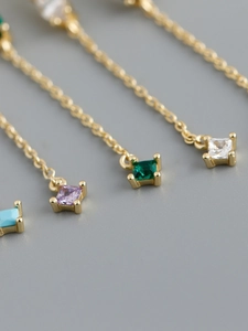 Dettaglio di pendenti in zircone quadrato colorato su nappe dorate con castone a quattro griffe