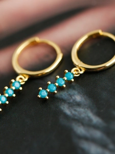 Vue macro de créoles dorées avec des pierres bleu turquoise suspendues verticalement