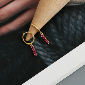 Détail de créoles dorées avec pendentifs sertis de pierres précieuses rondes roses et rouges