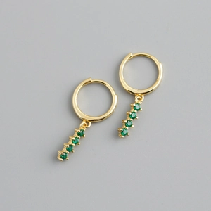 Détail de boucles d'oreilles créoles dorées avec pendentifs en zircons verts alignés