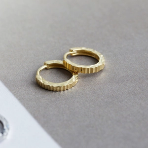 Primer plano de aretes de aro en plata S925 con facetas geométricas y acabado dorado