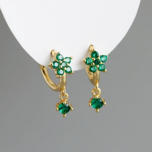 Détail macro de boucles d'oreilles fleur dorées avec zircons verts et pendentif