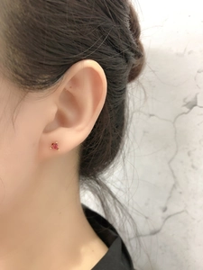 Détail d'une boucle d'oreille triangle en zircon rouge avec monture dorée portée