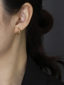 Close-up of elegant gold twisted hoop earrings worn on a model with premium lighting