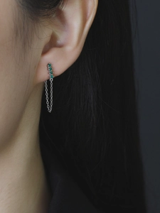 Detail of silver drop earrings with green cubic zirconia and long chain tassels on ear