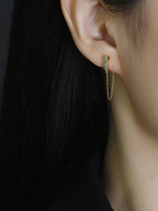 Close-up of gold chain earrings with three blue turquoise stones on model