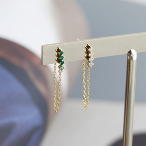 Close-up of asymmetric gold tassel earrings with vertical green and white cubic zirconia