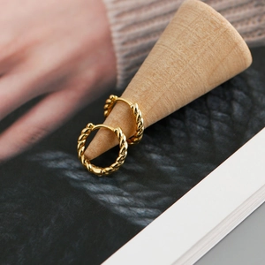 Macro detail of gold-plated twisted rope earrings on a wooden display stand
