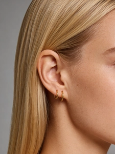 Primer plano de elegantes pendientes de aro dorados y pulidos en una modelo con estilo chic