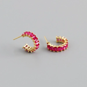 Detail of C-shaped gold hoop earrings with emerald-cut red zircon stones and studs
