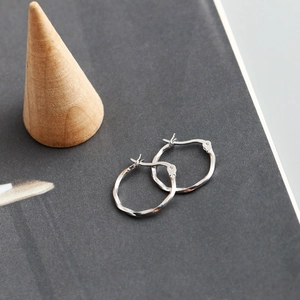 Detail van de gedraaide touwtextuur op zilveren oorringen op een houten displaystand