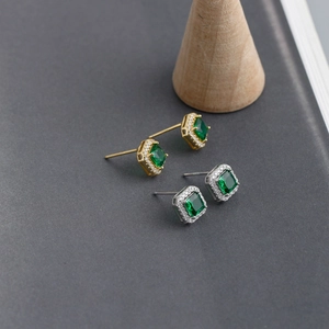 Close-up of square emerald halo stud earrings in gold and silver finishes on dark wood