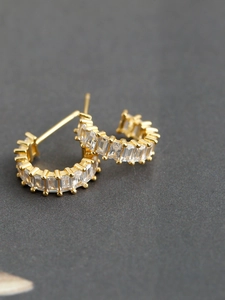 Close-up of gold-plated C-shaped earrings with baguette-cut cubic zirconia inlays