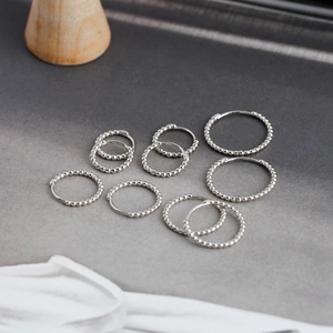 Macro detail of various sized S925 sterling silver beaded hoop earrings on a grey background