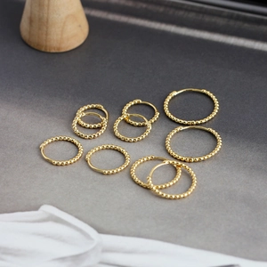 Macro view of assorted gold beaded hoop earrings set on a textured neutral background