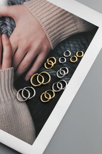 Macro detail of various sizes of polished gold and silver hoop earrings on a textured background