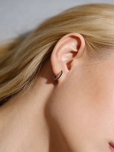 Gros plan d'une boucle d'oreille huggie en argent s925 doré avec zircons noirs incrustés
