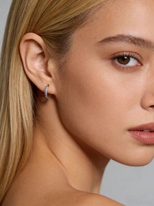 Gros plan d'une boucle d'oreille anneau dorée avec zircons bleus sur le lobe