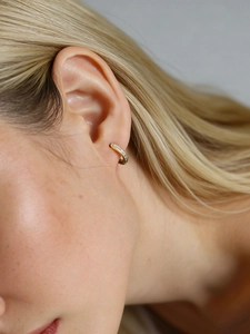 Gros plan d'une créole en argent s925 doré avec zircons colorés sur une oreille