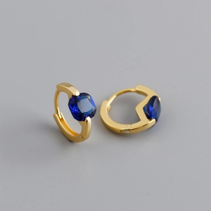 Vista macro di orecchini huggie in oro 18K con uno zircone blu scuro a taglio quadrato