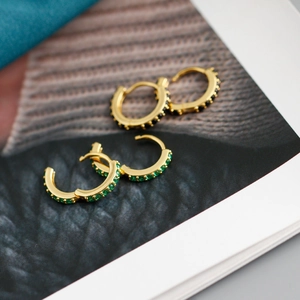 Détail de boucles d'oreilles huggies en argent s925 doré avec zircons noirs et émeraudes