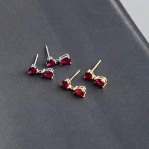 Detail of teardrop red zircon earrings in silver and gold plating on grey background