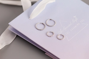 Primer plano de aretes de aro de plata 925 con textura trenzada sobre fondo de regalo
