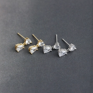 Detail of drop-shaped zircon stud earrings in gold and silver with four-prong settings