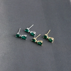 Close-up of green teardrop zircon earrings in silver and gold settings on a grey surface