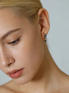 Detail of gold butterfly hoop earring with blue zircons worn on model's ear
