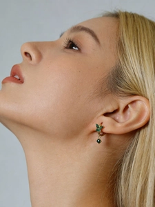 Detailed close-up of golden butterfly earrings with green stones on female model's ear